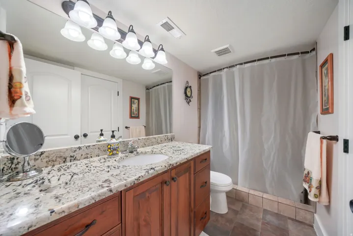 Granite-finish countertop with an integrated sink, wood-finish cabinetry, and a full-width mirror with a multi-bulb vanity light fixture