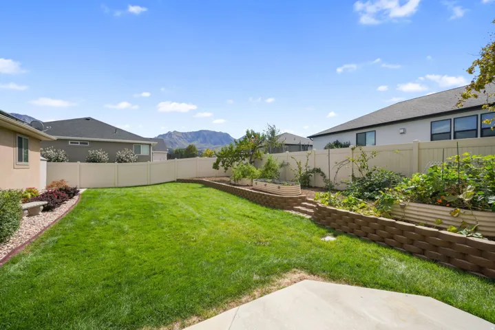 Expansive backyard featuring a manicured lawn, established garden beds, and a perimeter privacy fence