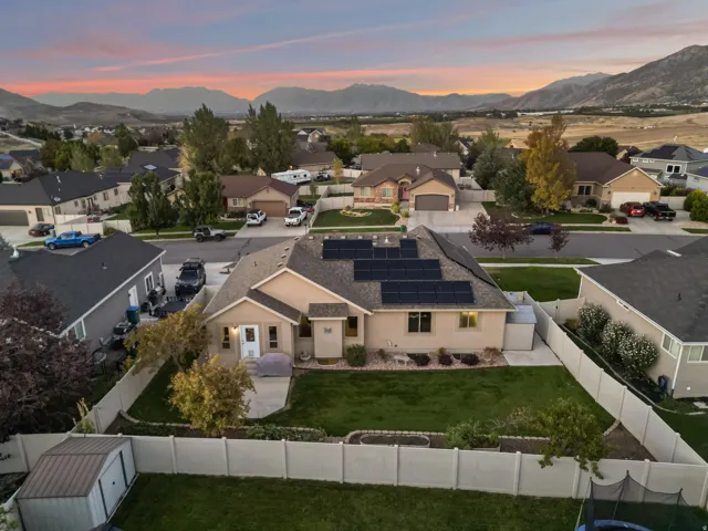 Single-story residence featuring a neutral exterior, a fenced backyard with a lawn, and a roof-mounted solar panel array