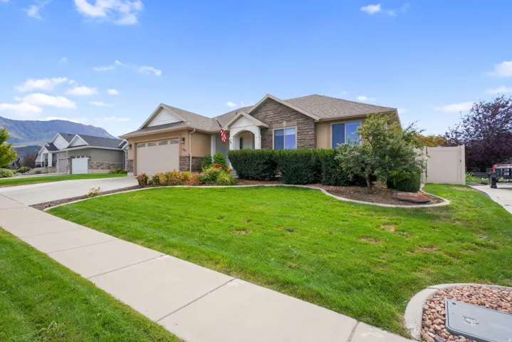Stone and stucco exterior with an attached two-car garage, mature landscaping, and a fenced side yard