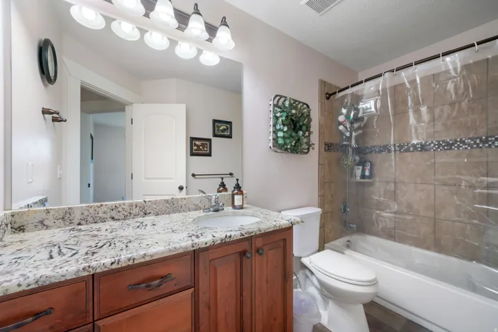 Granite-style countertop with an undermount sink, wood-finish cabinetry, and a full vanity mirror