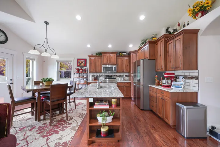 Kitchen featuring wood-finish flooring, recessed lighting, wood cabinetry, stainless steel appliances, and a granite-topped kitchen island with an integrated sink