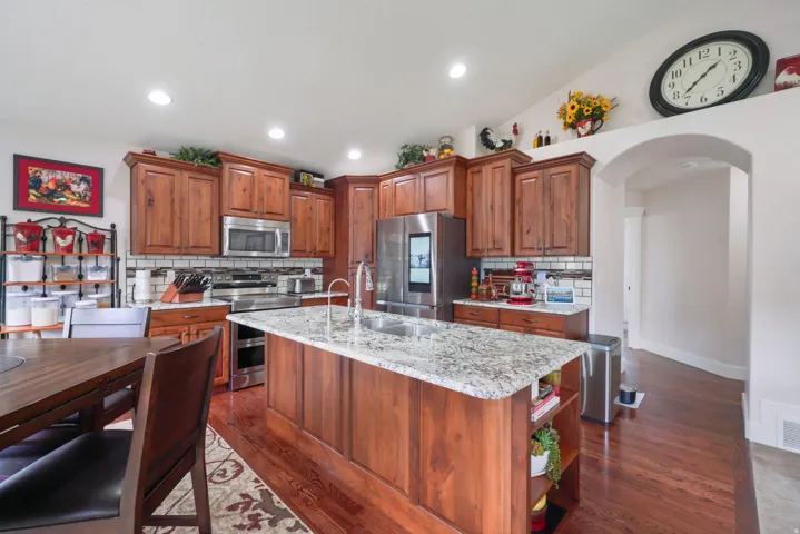 Kitchen featuring wood-finish cabinetry, stainless steel appliances, a large center island with a stone countertop, recessed lighting, and wood-finish flooring