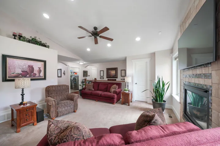 Vaulted ceilings with recessed lighting and ceiling fan, tiled fireplace with hearth, and light-toned carpeting throughout