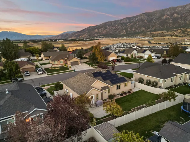 Property featuring a pitched roof, solar panel array, attached garage, and a fenced backyard
