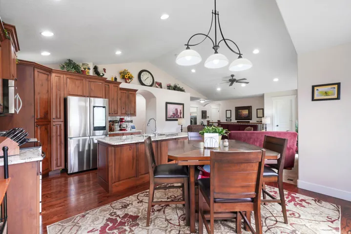 Vaulted ceiling, recessed lighting, wood-finish flooring, stainless steel refrigerator, and wood cabinetry with stone countertops
