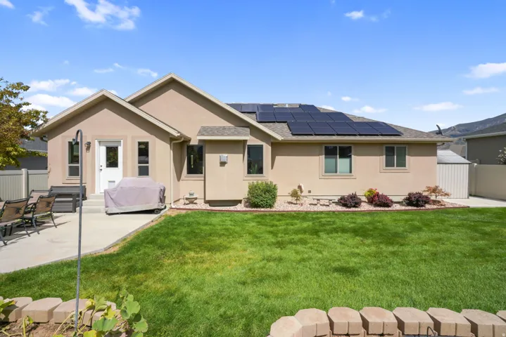 Stucco exterior with a pitched roof, solar panel array, concrete patio, and a landscaped yard featuring a retaining wall