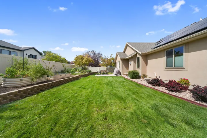Expansive lawn with mature landscaping, solar panels, stucco exterior, and raised garden beds with a block retaining wall