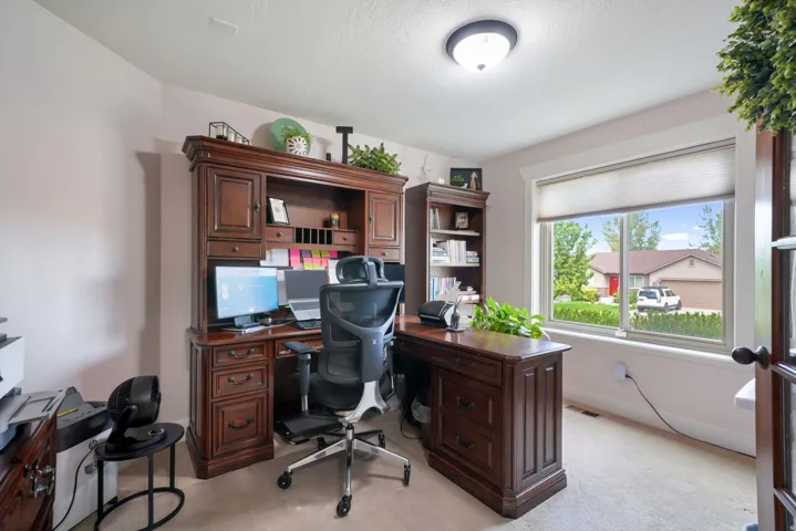 Built-in desk hutch with storage, window with exterior scenery, overhead flush-mount lighting, and carpet flooring
