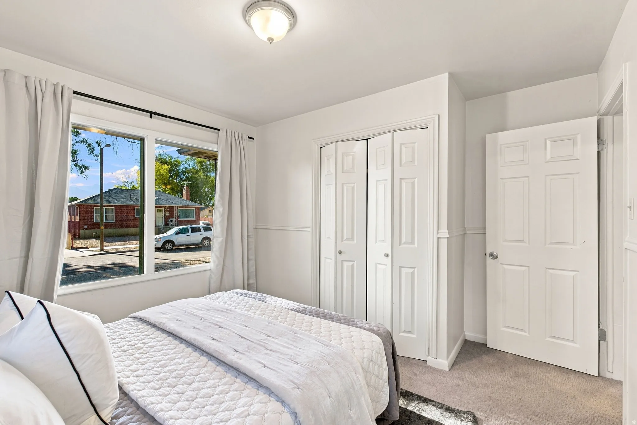 Recessed ceiling light fixture, white paneled bifold doors, window with dark curtain rod, white paneled door, and carpet flooring