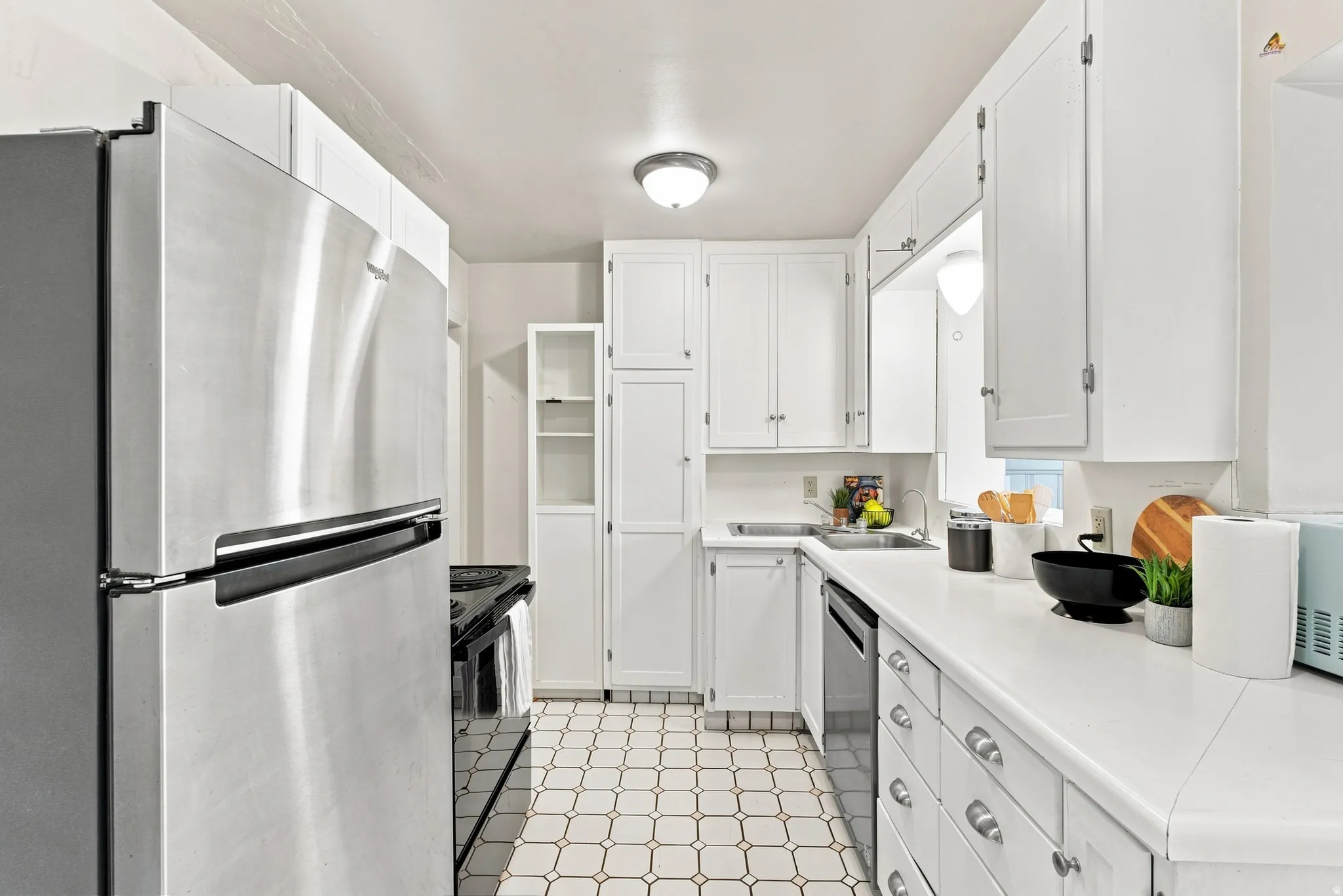 White kitchen cabinetry, stainless steel refrigerator, white countertops, built-in dishwasher, and patterned floor tiling
