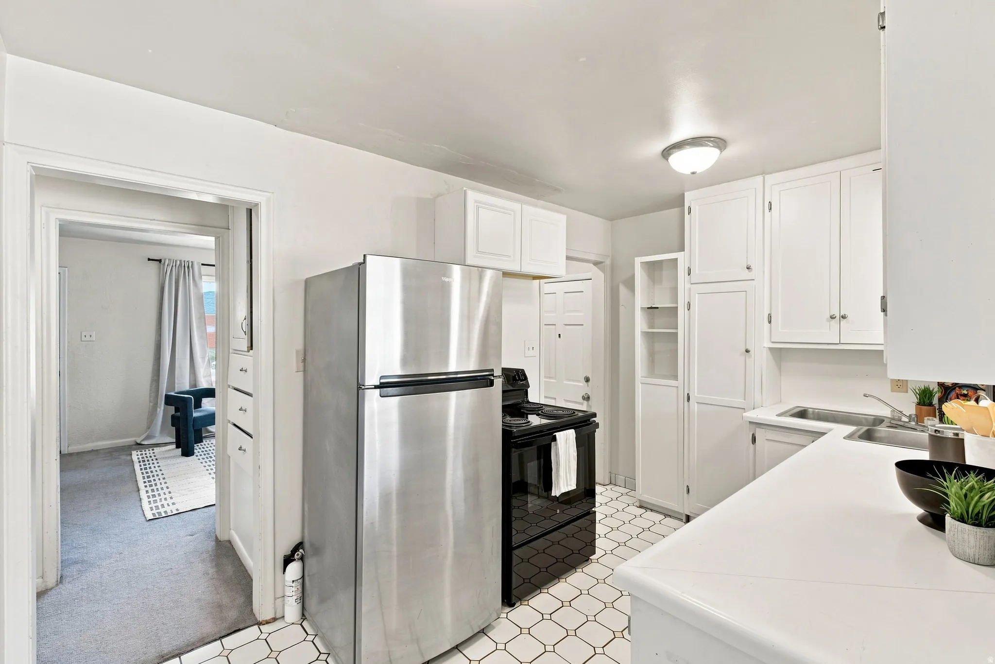 Stainless steel refrigerator, white cabinetry, black range, dual basin sink, and patterned floor tile