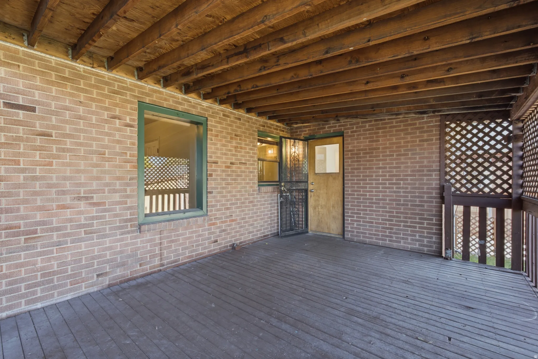 Covered outdoor deck with exposed wood beam ceiling, wood-finish flooring, brick exterior walls, and lattice paneling