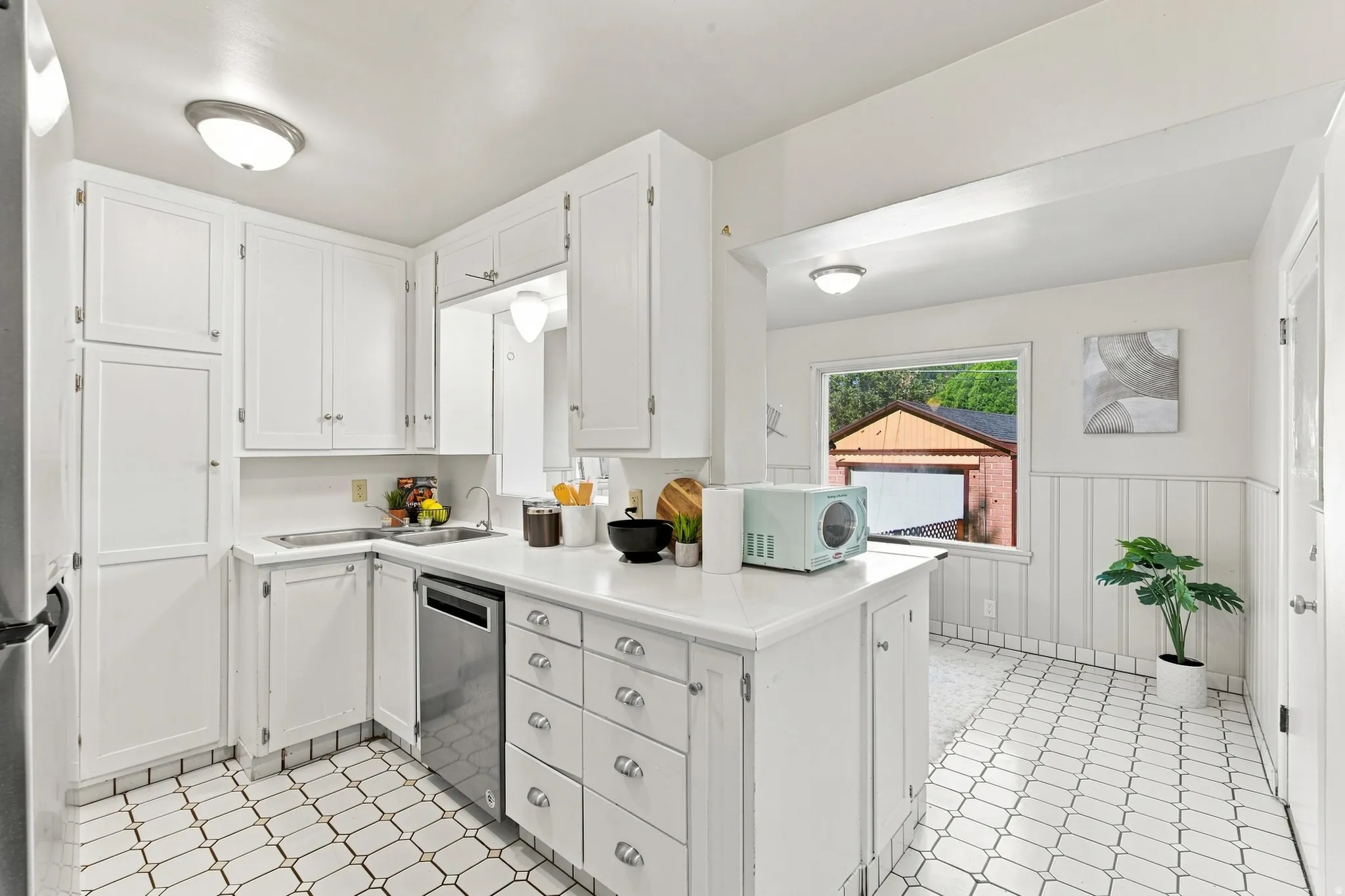 Kitchen featuring white cabinetry, stainless steel dishwasher, white countertops, and patterned tile flooring