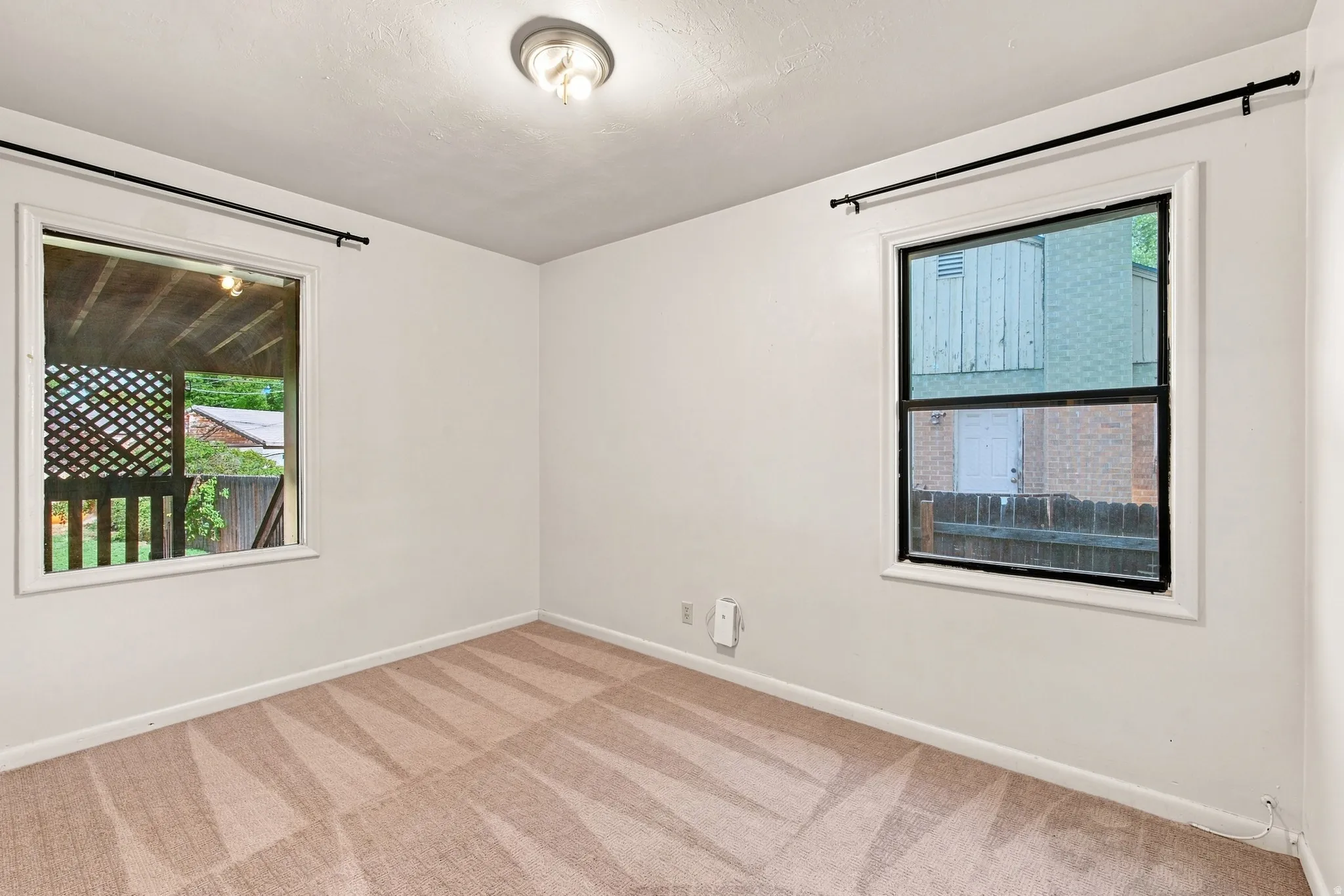 Recessed ceiling light fixture, white painted walls, two windows with black trim, and patterned carpet