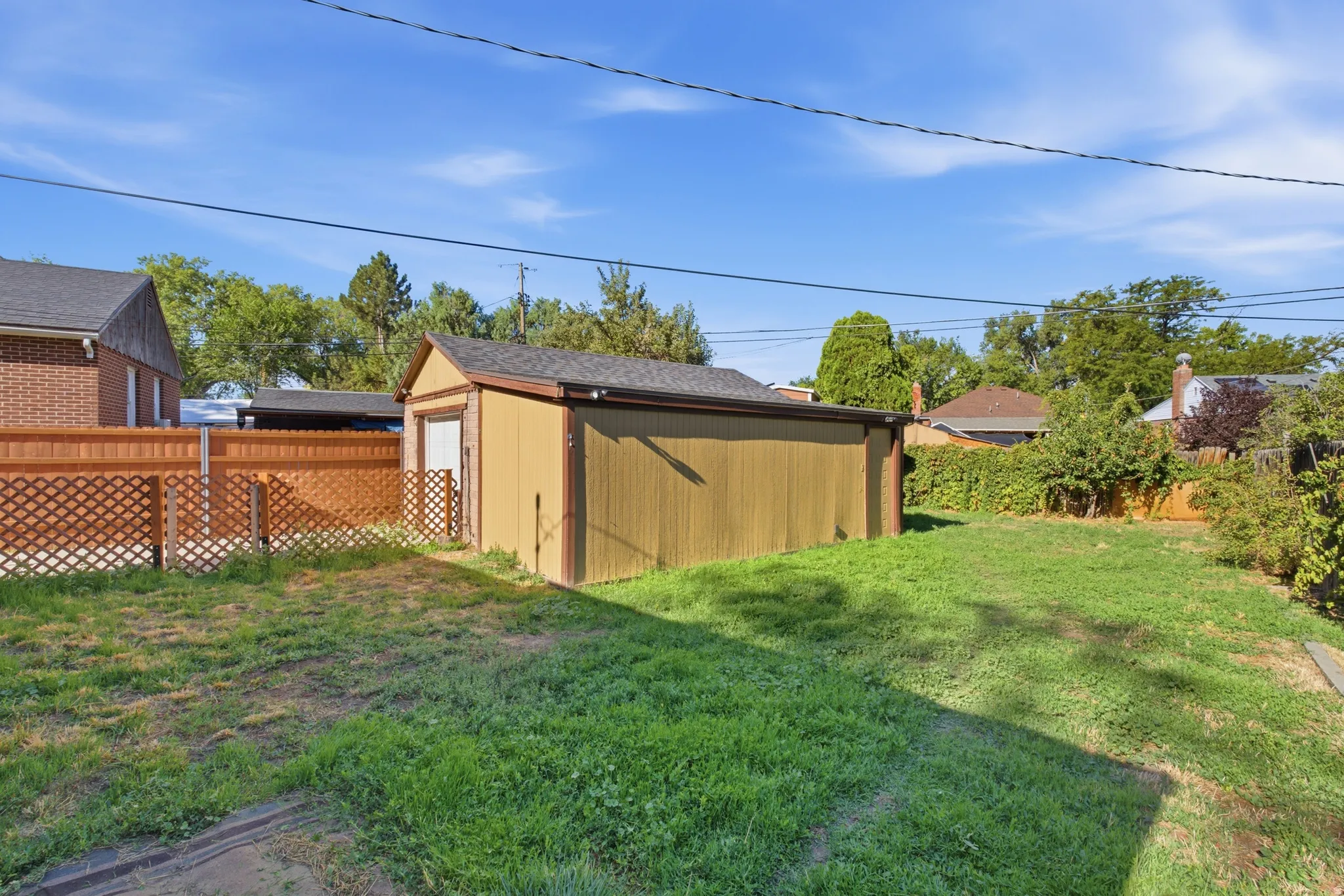 Expansive yard featuring a detached auxiliary structure, wood fencing with lattice detail, and mature perimeter landscaping