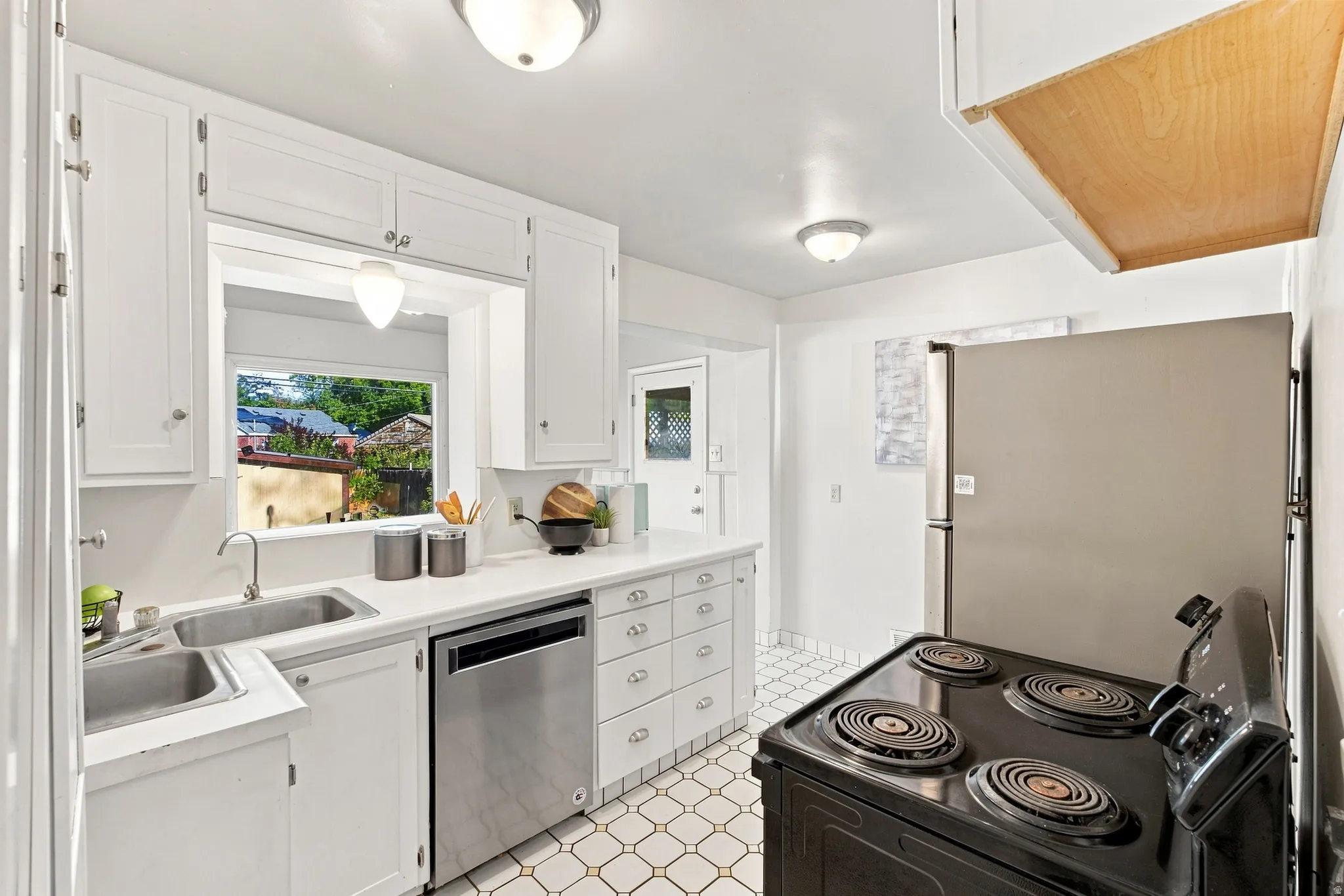 White cabinetry, stainless steel double basin sink, white countertops, built-in dishwasher, and patterned floor tile
