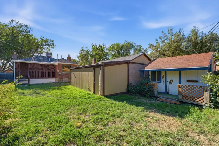 Expansive grassy yard with a covered patio, two detached accessory structures, and mature perimeter landscaping