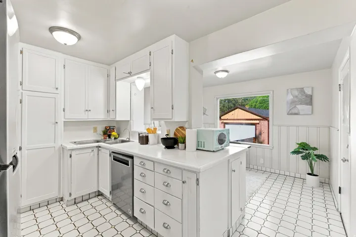 Kitchen featuring white cabinetry, stainless steel dishwasher, white countertops, and patterned tile flooring