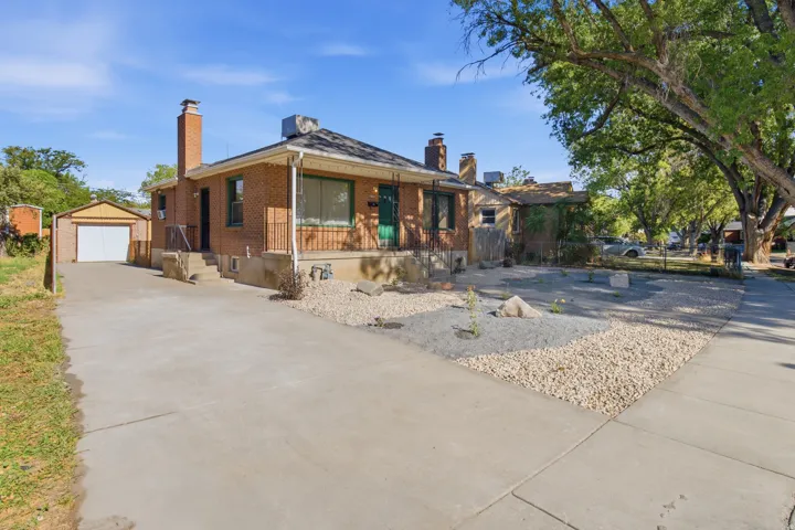 Brick exterior with a covered porch, an attached garage, a concrete driveway, and a xeriscaped front yard