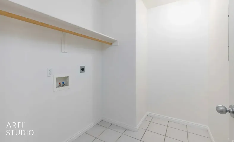 Utility area featuring tile flooring, a white wall shelf, and laundry hookups