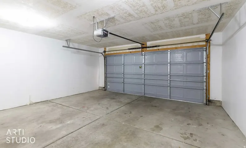 Concrete flooring with visible expansion joints, white painted walls, and a paneled garage door