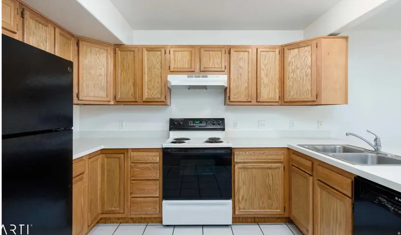 U-shaped kitchen featuring wood cabinetry, white countertops, white tile flooring, a black refrigerator, and a black and white electric range