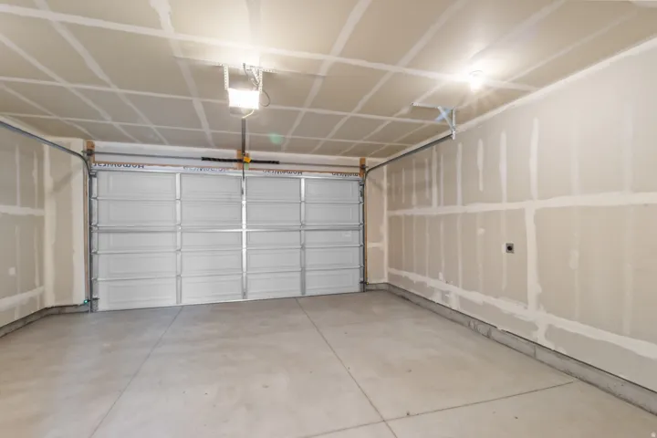 Spacious two-car garage with a concrete floor, an overhead door, and exposed wall framing