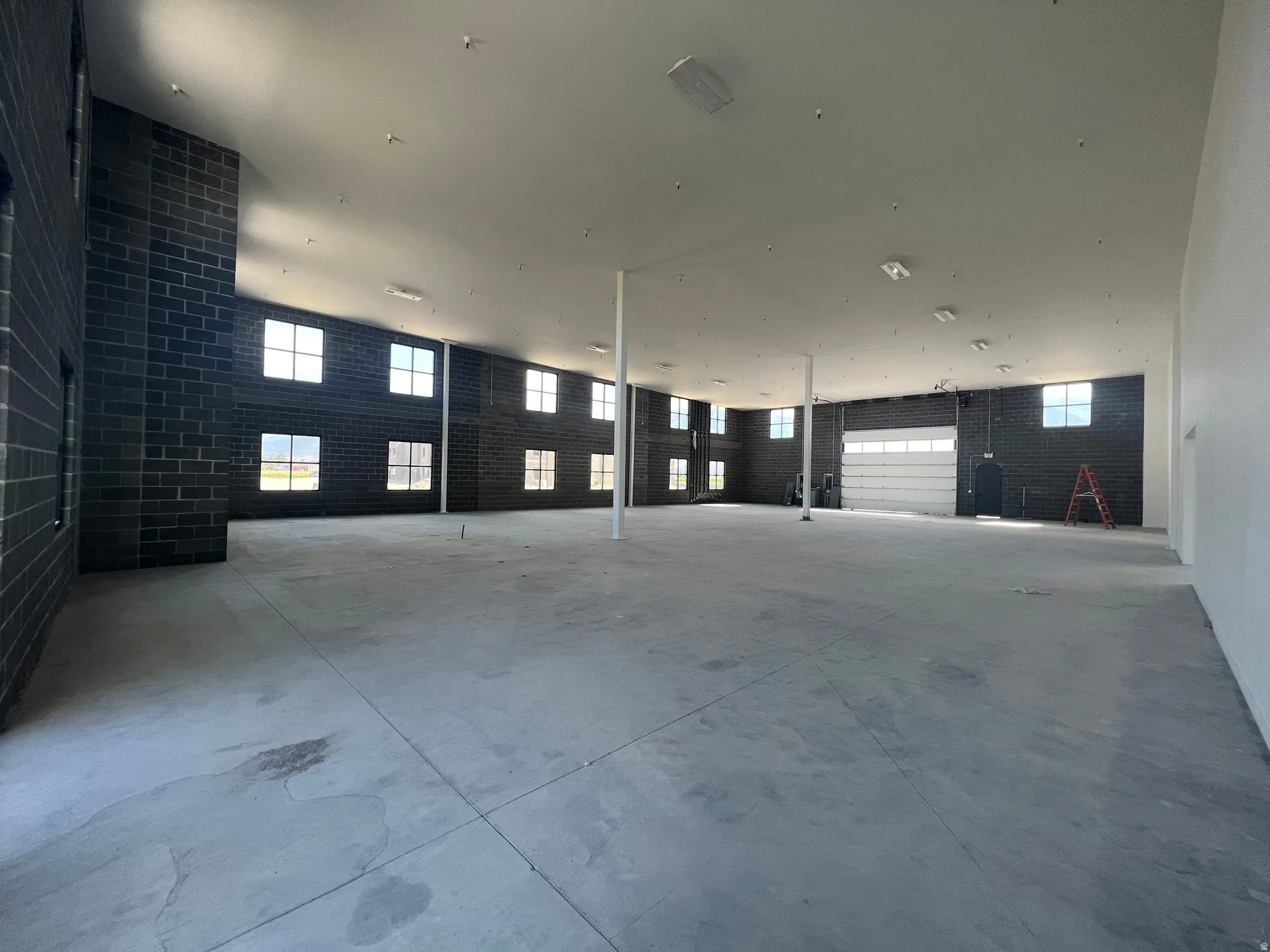 Expansive open floor plan with concrete flooring, high ceilings, multiple windows, and a roll-up door
