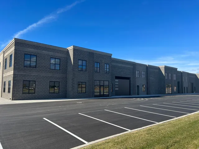 Modern commercial building featuring a block exterior, multiple window units, a large roll-up door, and an expansive paved parking area with marked spaces