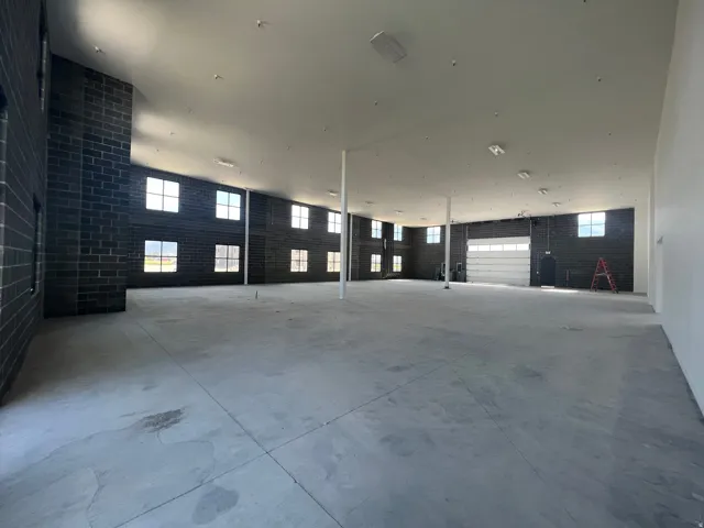 Expansive open floor plan with concrete flooring, high ceilings, multiple windows, and a roll-up door
