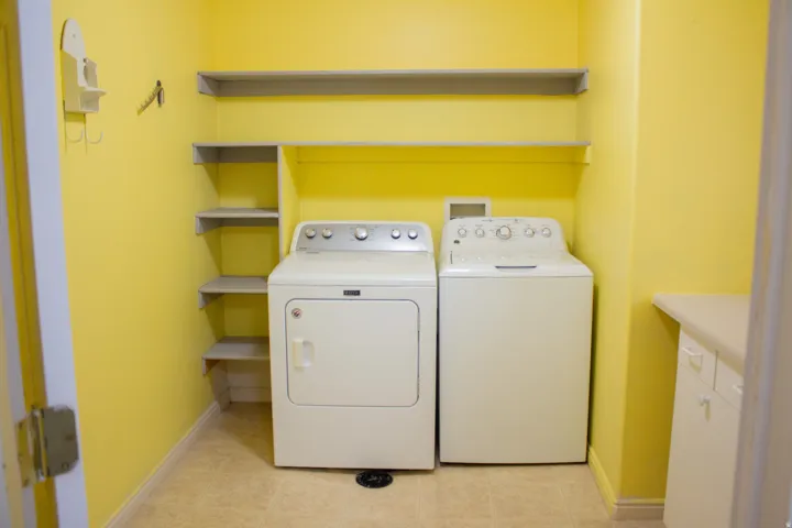 Dedicated laundry area featuring the included washer and dryer, floor drain, integrated shelving, and a built-in cabinet with countertop. Laminate flooring
