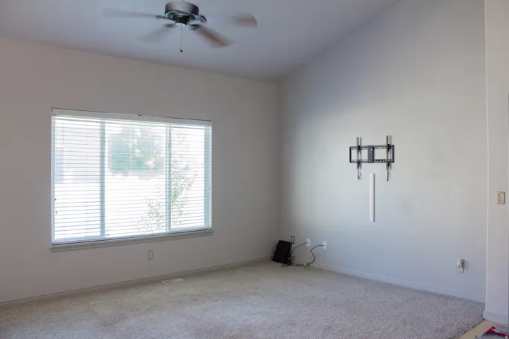 Vaulted ceiling, ceiling fan, large window with blinds, carpeted flooring, built-in tv wall mount
