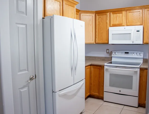 Kitchen with light wood cabinetry, and light-toned countertops. Pantry next to the refrigerator. All kitchen appliances included (refrigerator, electric range, and microwave)
