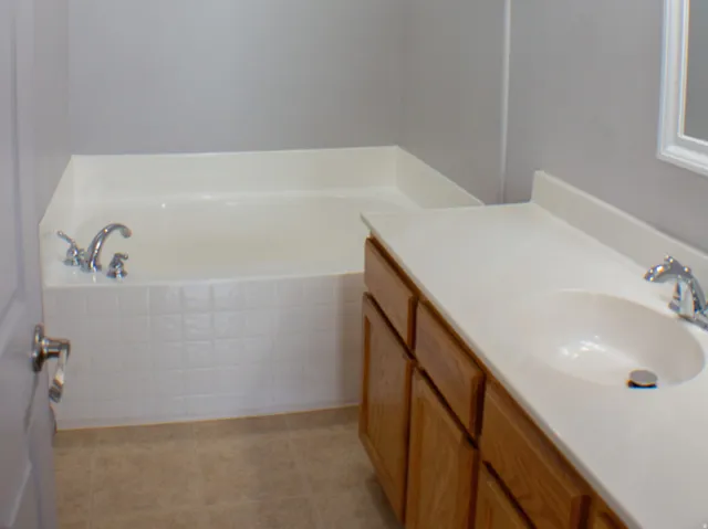 Primary bathroom. Built-in bathtub, wood-finish vanity with single sink, laminate flooring