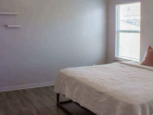 Primary bedroom located off the dining area. Vaulted ceiling featuring a ceiling fan with integrated lighting, laminate flooring, two windows, and floating shelves.