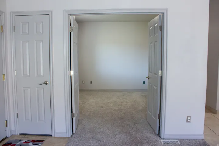 Office space with double door opening, carpeted flooring. Closet next to office.