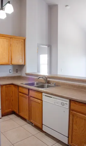 Kitchen featuring wood-finish cabinetry, a double basin stainless steel sink, a white dishwasher, and tile flooring