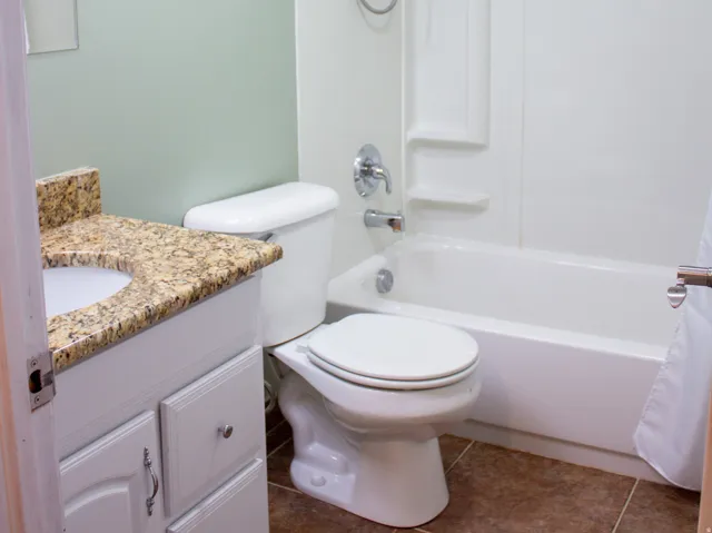 Bathroom featuring a white vanity with a stone countertop and integrated sink, a white toilet, and a white tub with shower. Tile flooring.