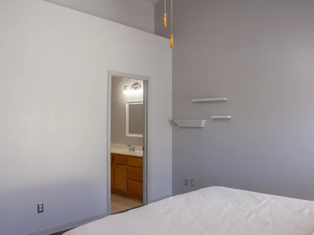 Primary bedroom. Vaulted ceiling with a ceiling fan, wall-mounted floating shelving, and laminate flooring