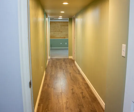 Hallway leading from the landing featuring laminate flooring, and recessed lighting. Walls are the same light green as the basement family room and basement bathroom.