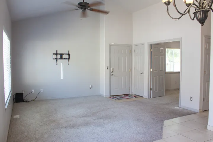 Vaulted ceilings with a ceiling fan, light-toned carpeting, and a built-in tv wall mount