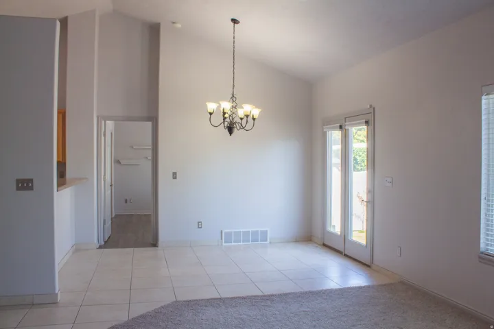 Vaulted ceiling, chandelier, tiled flooring, and doors with blinds leading to the backyard.