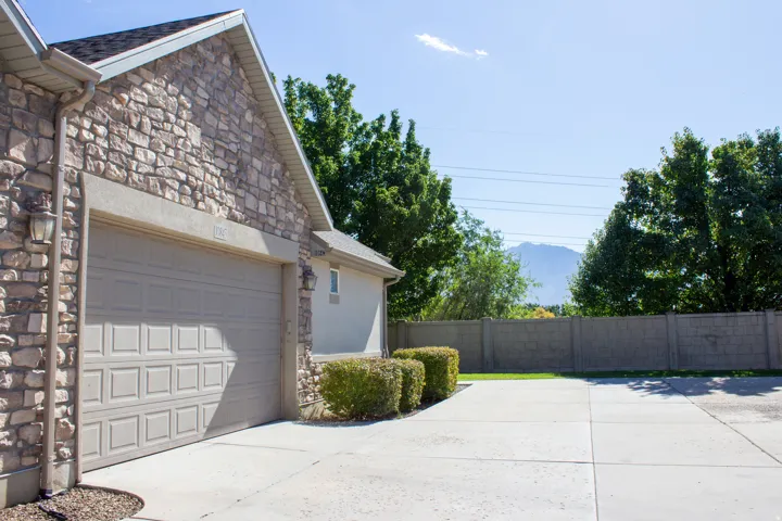 Stone veneer exterior with an attached 2 garage, concrete driveway with extra parking space, and mature landscaping