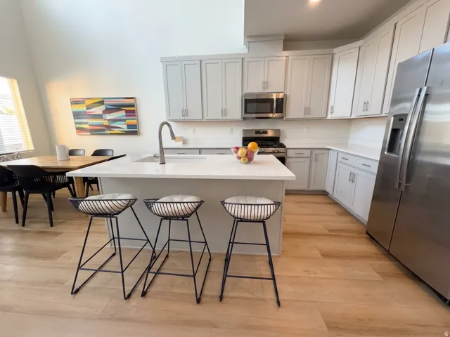 Spacious kitchen featuring an island with an integrated sink, light-toned cabinetry, stainless steel appliances, and wood-finish flooring