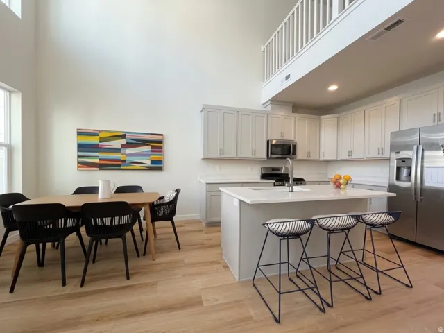 Open-concept living space featuring high ceilings, wood-finish flooring, a contemporary kitchen with light-toned cabinetry, and a large central island with a sink