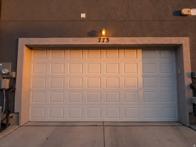 Panel garage door with stucco exterior, exterior wall-mounted light fixture, and concrete driveway