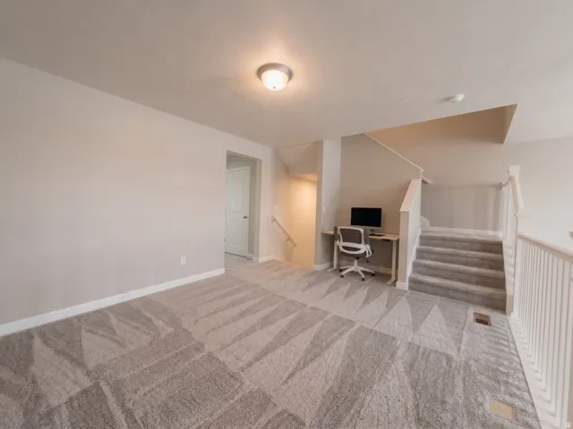 Carpeted landing area featuring a staircase with white balusters, a ceiling-mounted light fixture, and neutral wall tones