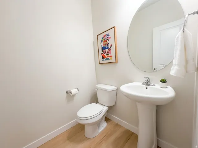 Pedestal sink with chrome faucet, oval wall mirror, and wood-finish flooring