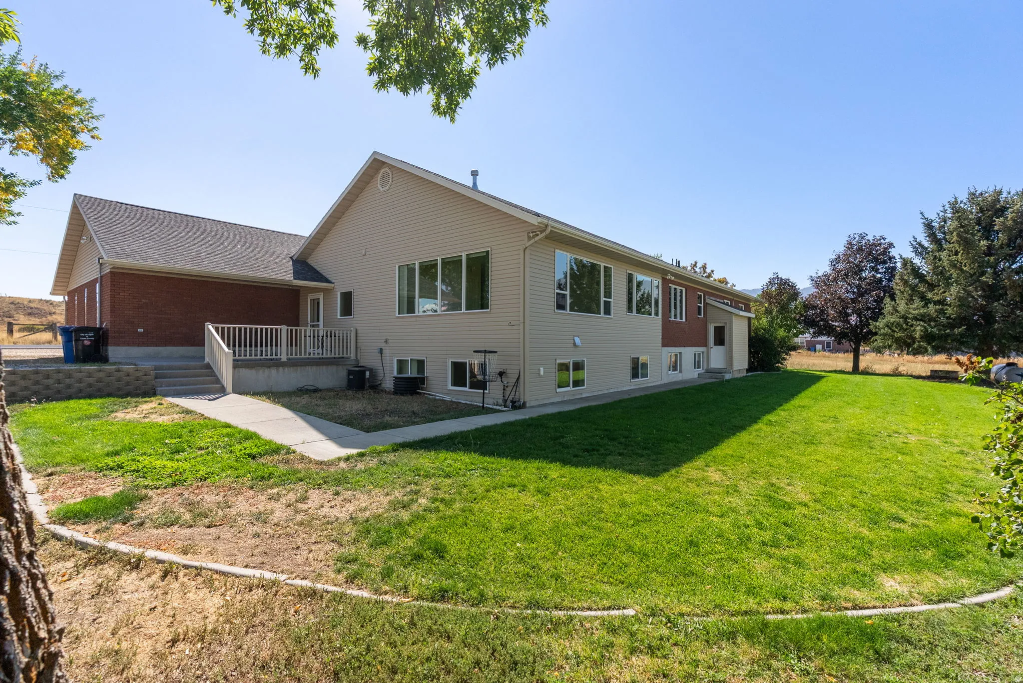 Spacious rear yard with a manicured lawn, an elevated deck with white railing, and a side patio with steps